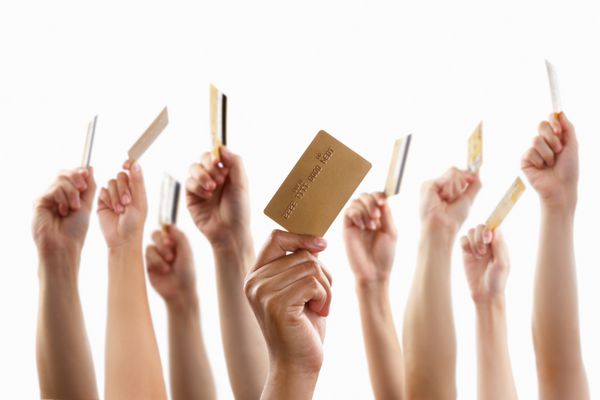 دست های زیادی که کارت اعتباری طلایی را بالا می برند و در دست دارند در برابر پس زمینه سفید