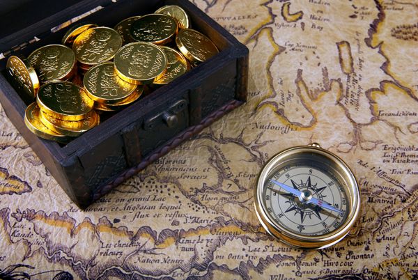 قطب نما برنجی قدیمی روی یک نقشه بسیار قدیمی با صندوقچه گنج پر از سکه های طلایی قرار گرفته است