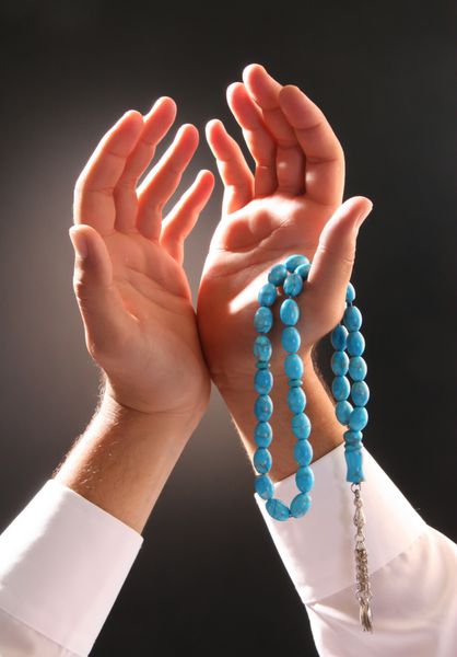 دست مردی که تسبیح را در حالت دعا و درخواست در دست گرفته است