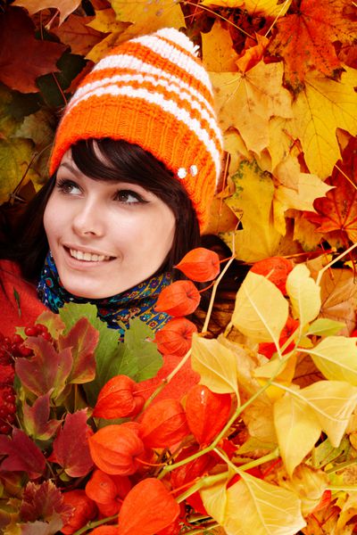دختری با کلاه نارنجی پاییزی روی گروه برگ با گل فضای باز