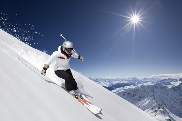اسکی باز زن در حال اسکی در سراشیبی با آفتاب و کوه