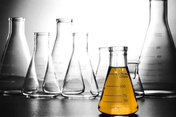 فلاسک ارلن مخروطی شیشه ای آزمایشگاهی پر از مایع بنزینی زرد رنگ برای آزمایش در آزمایشگاه تحقیقات علمی