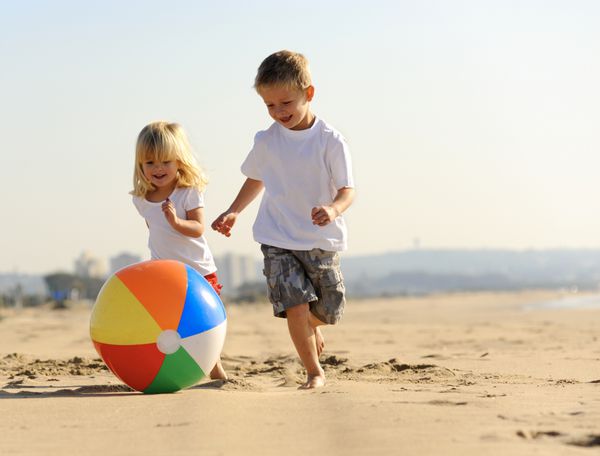برادر و خواهر زیبا با توپ ساحلی در فضای باز بازی می کنند