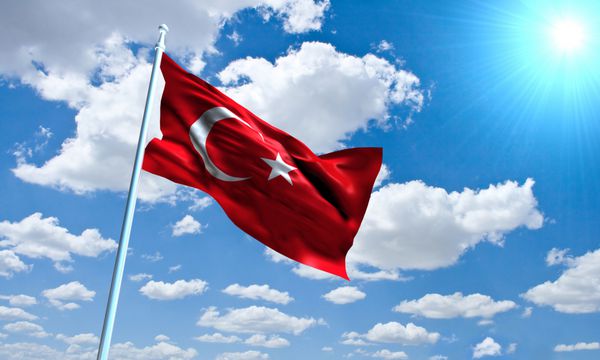 پرچم ترکیه در مقابل آسمان روشن آفتابی و ابری