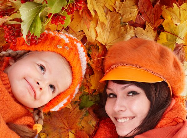خانواده شاد با فرزند روی برگ های نارنجی پاییزی فضای باز
