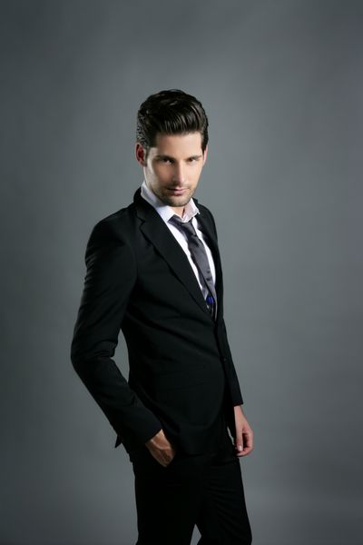 کراوات گاه به گاه کت و شلوار مشکی تاجر جوان مد در پس زمینه خاکستری
