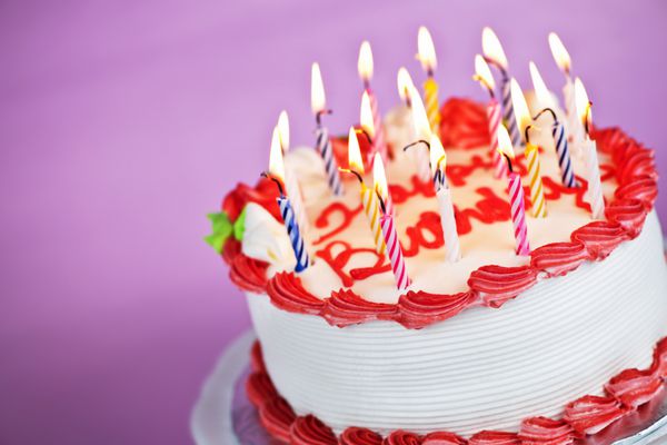 کیک تولد با شمع های سوزان روی بشقاب در پس زمینه صورتی