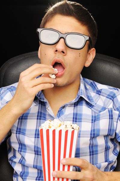 مرد جوان در حال تماشای فیلم با عینک سه بعدی در سینما