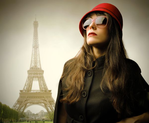زن زیبا با عینک آفتابی مد روز و کلاه با برج ایفل در پس زمینه