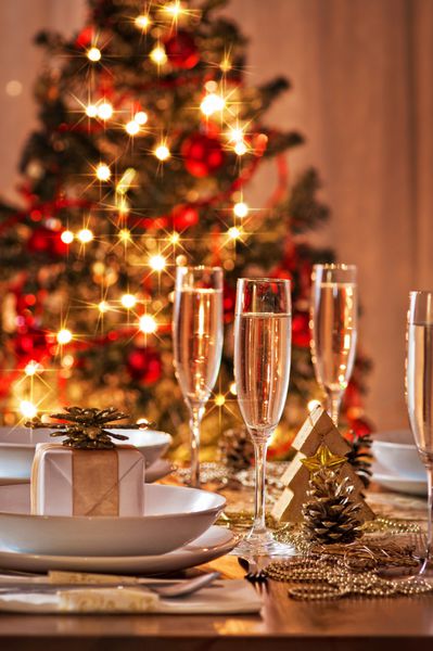 میز ناهار خوری کریسمس تزئین شده با لیوان های شامپاین و درخت کریسمس در پس زمینه