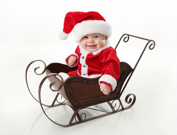 کودک خردسال شایان ستایش با کت و شلوار بابا نوئل و کلاهی که در یک سورتمه برفی کریسمس فلزی نشسته است