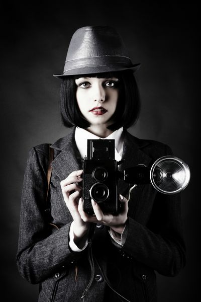 زن زیبای جوان با ظاهر رترو که یک دوربین قدیمی قدیمی در دست دارد