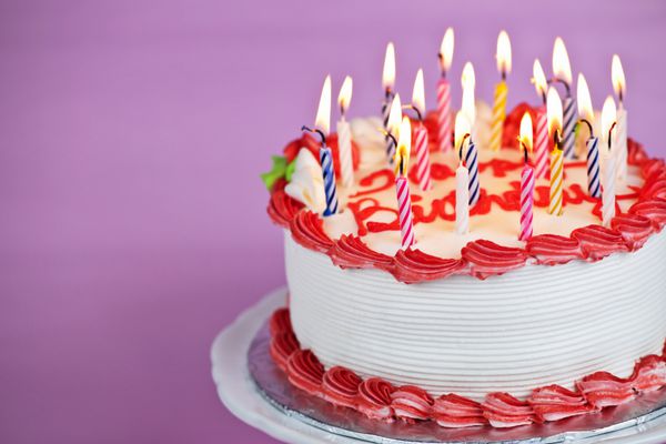 کیک تولد با شمع های سوزان روی بشقاب در پس زمینه صورتی