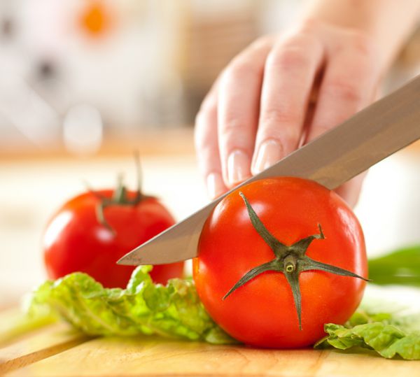 دستان زن در حال بریدن گوجه فرنگی پشت سبزیجات تازه
