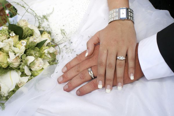 زوج عاشقی که با حلقه هایی در مقابل لباس عروس دست در دست گرفته اند