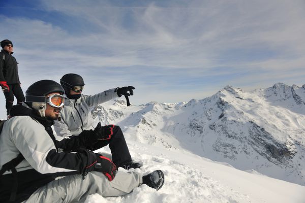 گروه افراد شاد در فصل زمستان روی برف در کوه با آسمان آبی و هوای تازه سرگرم می شوند