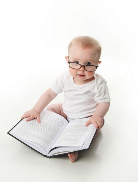 پرتره یک نوزاد شایان ستایش نشسته با عینک و نگاه کردن به کتاب جدا شده روی سفید