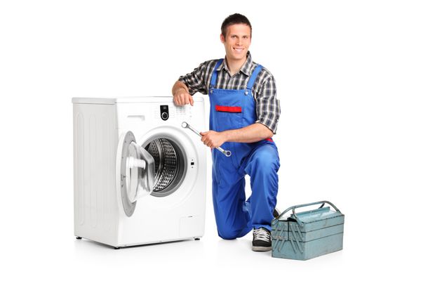 تعمیرکاری که یک آچار در دست دارد و در کنار ماشین لباسشویی ایزوله شده روی پس زمینه سفید عکس گرفته است