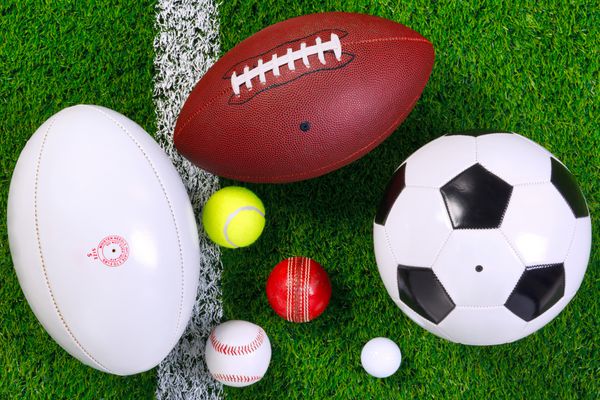 عکس توپ های ورزشی مختلف روی چمن کنار خط سفید که از بالا شلیک شده است