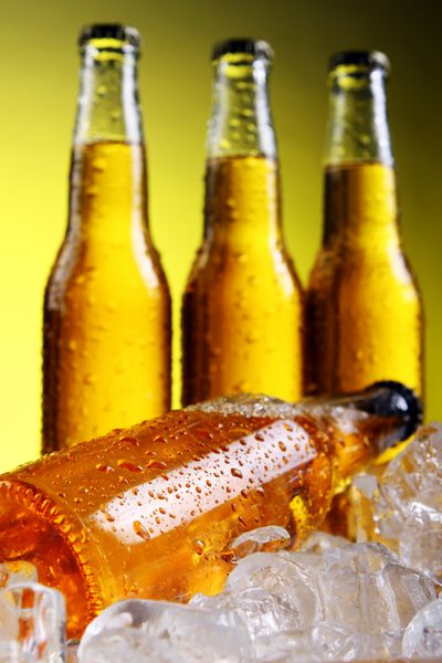 بطری های آبجو سرد و تازه با یخ روی پس زمینه زرد