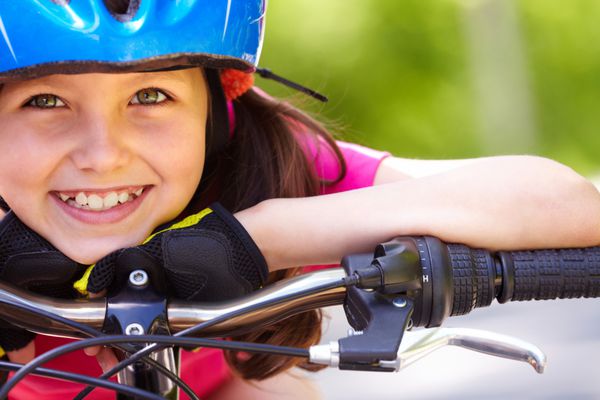 نمای نزدیک از صورت دختر بچه ای که با دوچرخه به دوربین نگاه می کند و لبخند می زند