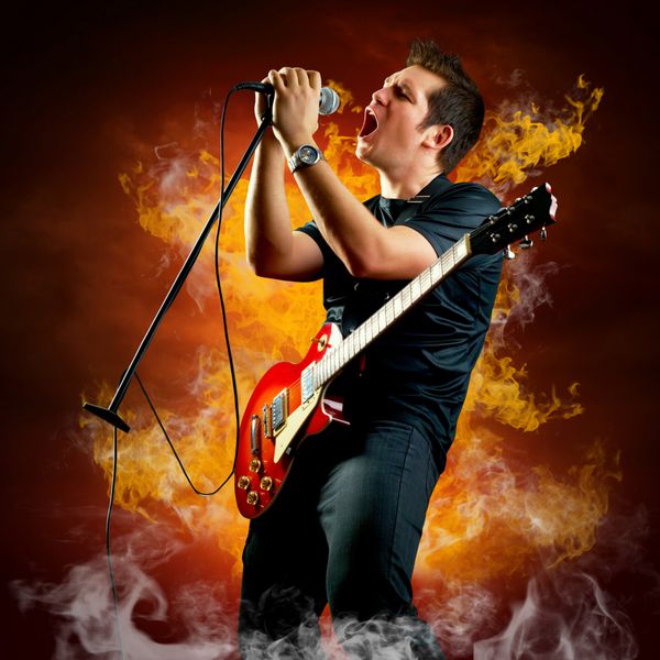 گیتاریست راک با گیتار الکتریک در اطراف شعله های آتش می نوازد