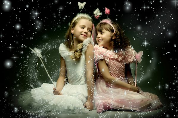 دو دختر کوچولوی زیبا با بال بنشینید و روی پس زمینه تاریک آسمان پرستاره لبخند بزنید