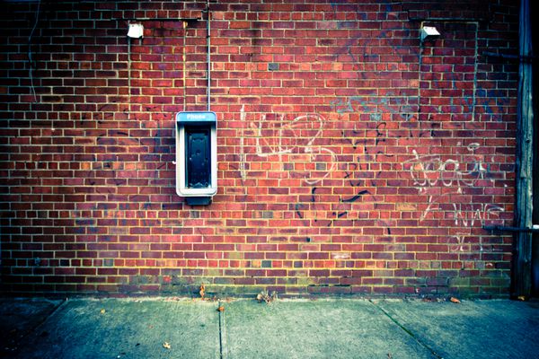 پس‌زمینه شهری غم‌انگیز از دیوار آجری با تلفن قدیمی غیرفعال روی آن