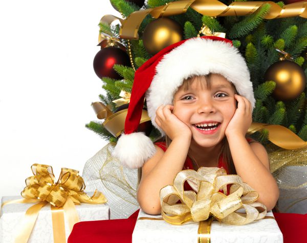 دختر کوچک زیبا با هدیه نزدیک درخت کریسمس لبخند می زند