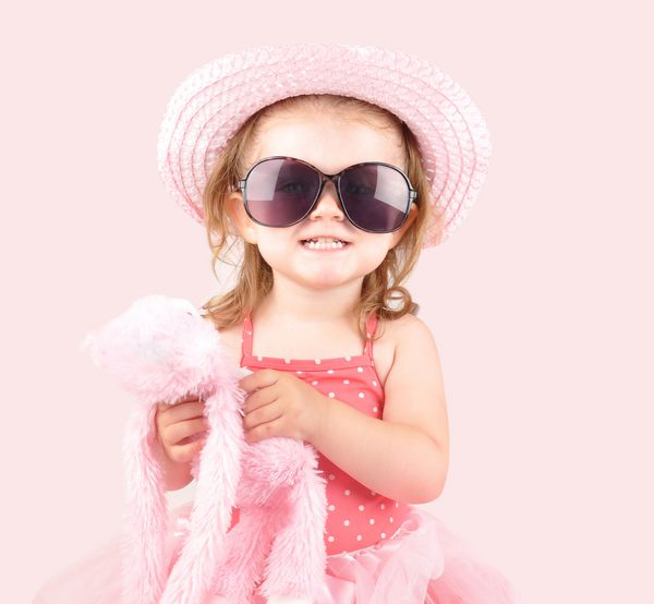 دختر کوچکی لباس صورتی با عینک آفتابی و کلاه پوشیده است از آن برای یک شاهزاده خانم یا مفهوم لباس استفاده کنید