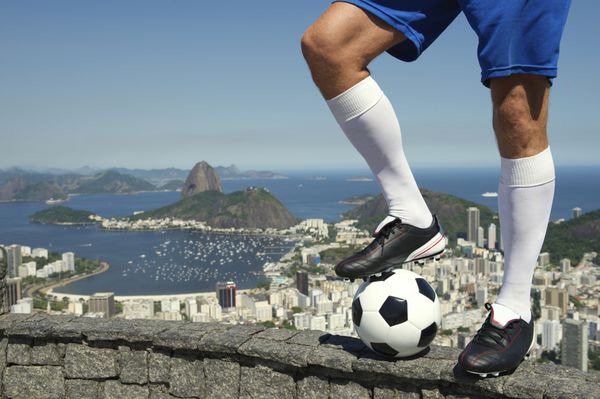 پای فوتبالیست برزیلی که با فوتبال بالای خط افق ریودوژانیرو با کوه شوگرلوف ایستاده است
