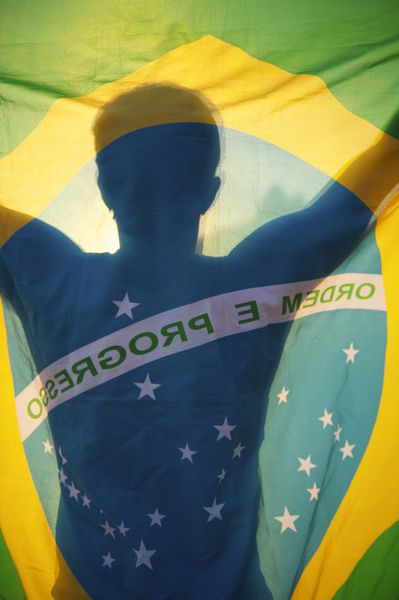 سایه مردی که پرچم برزیل را در غروب خورشید در دست دارد با کوه دو برادر در ریودوژانیرو برزیل