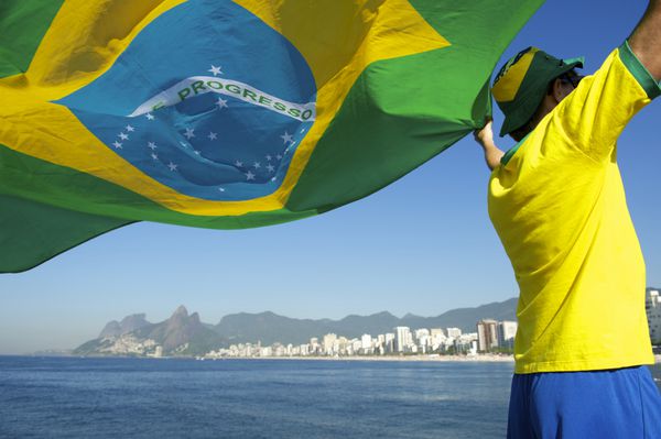بازیکن فوتبال برزیلی در حال اهتزاز پرچم در مقابل خط افق شهر ساحل ایپانما ریودوژانیرو برزیل