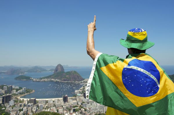 مردی در پرچم برزیل با انگشت شماره یک در مشرف به ریودوژانیرو ایستاده است