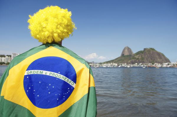 هوادار وطن پرست برزیلی ایستاده در پرچم پیچیده شده و به کوه شوگرلوف بوتافوگو نگاه می کند ریودوژانیرو برزیل