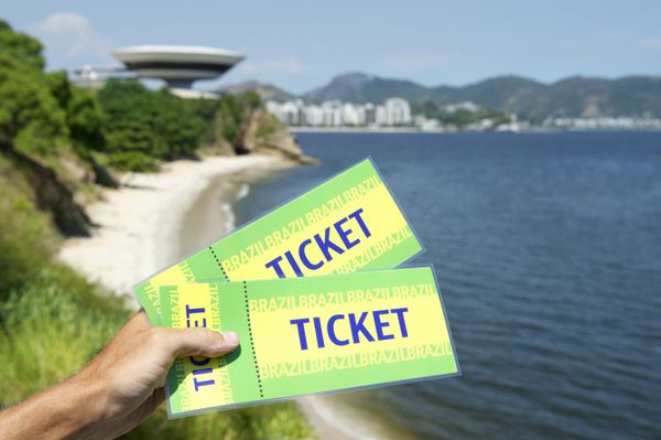 دست در دست گرفتن یک جفت بلیط برزیل در مقابل منظره زیبای نیتروی و خلیج گوانابارا ریودوژانیرو