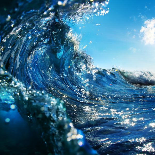 موج اقیانوس آبی رنگی چرخان که در زمان غروب آفتاب به پایین سقوط می کند