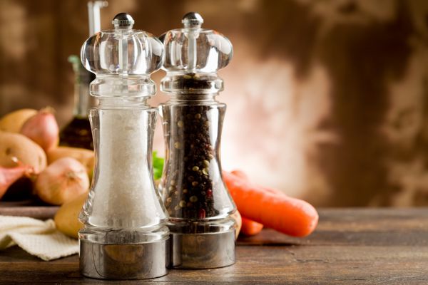 عکس آسیاب نمک و فلفل با مواد اولیه روی میز چوبی