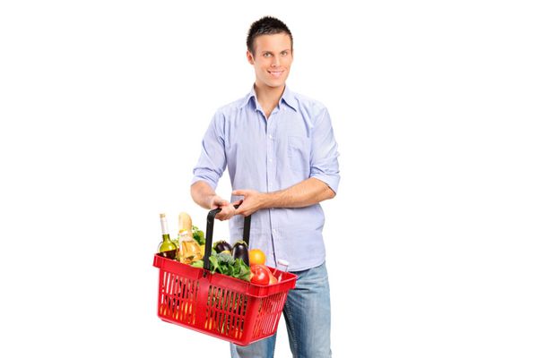 مرد جوانی که یک سبد خرید پر از محصولات جدا شده در پس زمینه سفید در دست دارد