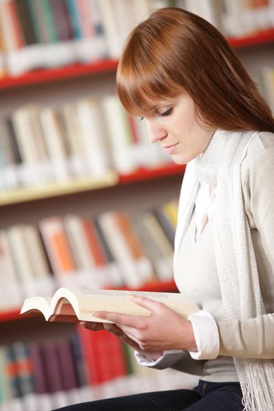 دانش آموز جوان در حال خواندن در کتابخانه
