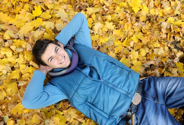 پرتره مرد جوان خندان در حال خوابیدن در شاخ و برگ در پارک پاییز فضای باز