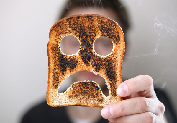 مردی که یک تکه نان تست سوخته با یک شکلک ناخوشایند برای شروع بد روز در دست گرفته است