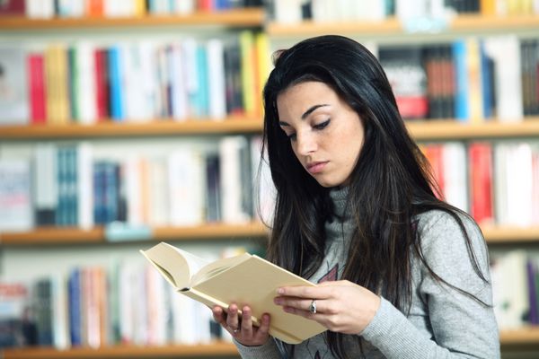 دانش آموز دختر در حال خواندن کتاب در کتابخانه