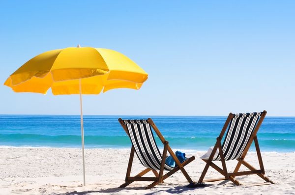 یک جفت صندلی آفتابگیر و یک چتر ساحلی در ساحلی متروک مفهوم کامل تعطیلات