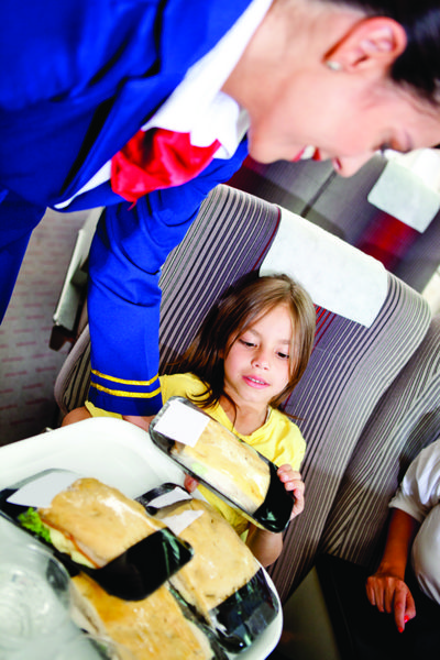 مهماندار هواپیما در حال سرو غذا برای بچه ای در هواپیما