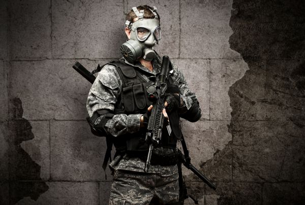 پرتره یک سرباز جوان با ماسک گاز و تفنگ در پس زمینه آجری گرانج