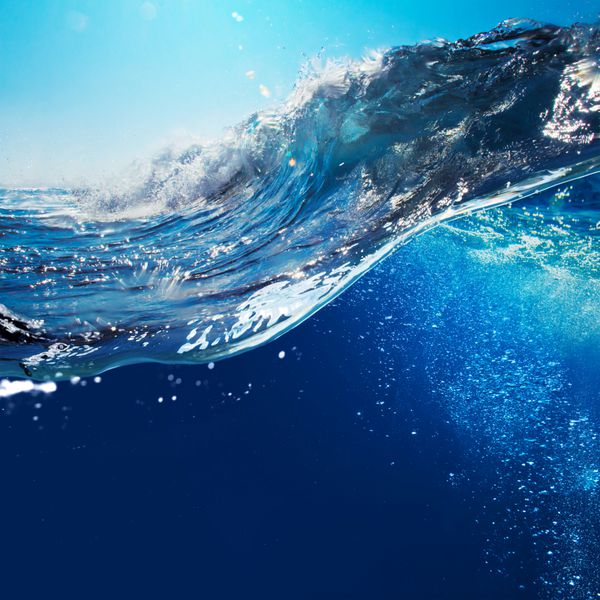 منظره دریا با منظره اقیانوس با آسمان آبی و نور خورشید موج بزرگ اقیانوس فرفری که توسط خط آب به قسمت زیر آب با حباب های هوا تقسیم شده است