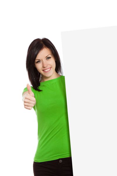 زن جوان با لبخند شاد ایستاده ایستاده تخته خالی را نگه دارد ژست انگشت شست به بالا دختر جذاب پیراهن سبز جدا شده روی پس زمینه سفید عکسبرداری استودیویی