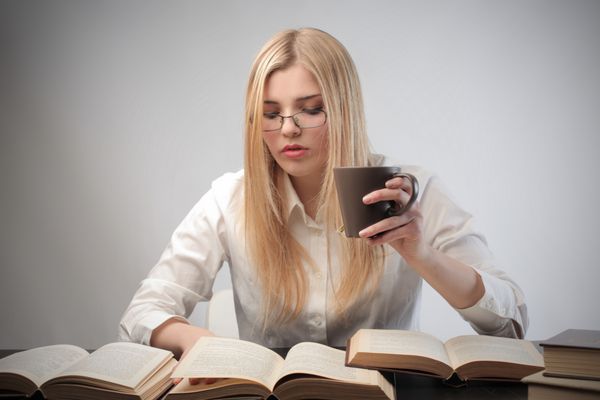 زن جوان در حال مطالعه در حال خوردن یک فنجان چای