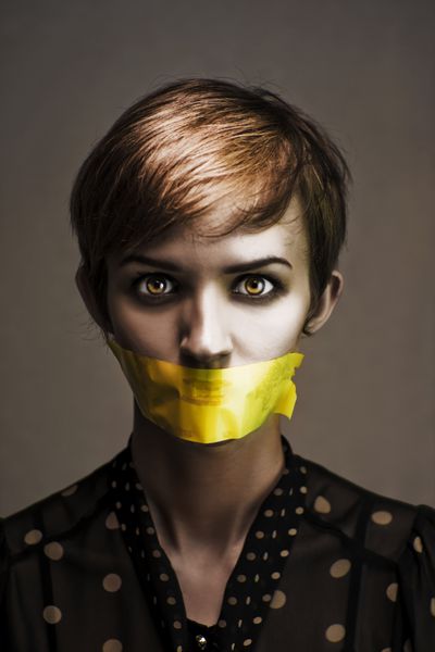 عکس تیره از یک زن مضطرب و مظلوم که در سکوت بسته شده و در سکوت خفه شده است با نوار ماسک زردی که دهانش را در یک سخنرانی بدون شرارت می پوشاند